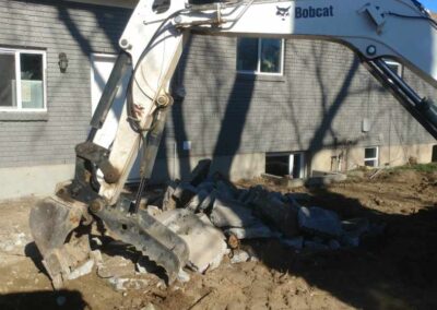 Using an excavator to remove an old, cracked, uneven concrete patio.